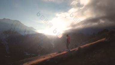 非常长的镜头鸟图, 一个女孩走在山边上, 在美丽的日落中作为一个剪影。一个戴帽子的女孩的剪影从山上下来的山坡上
